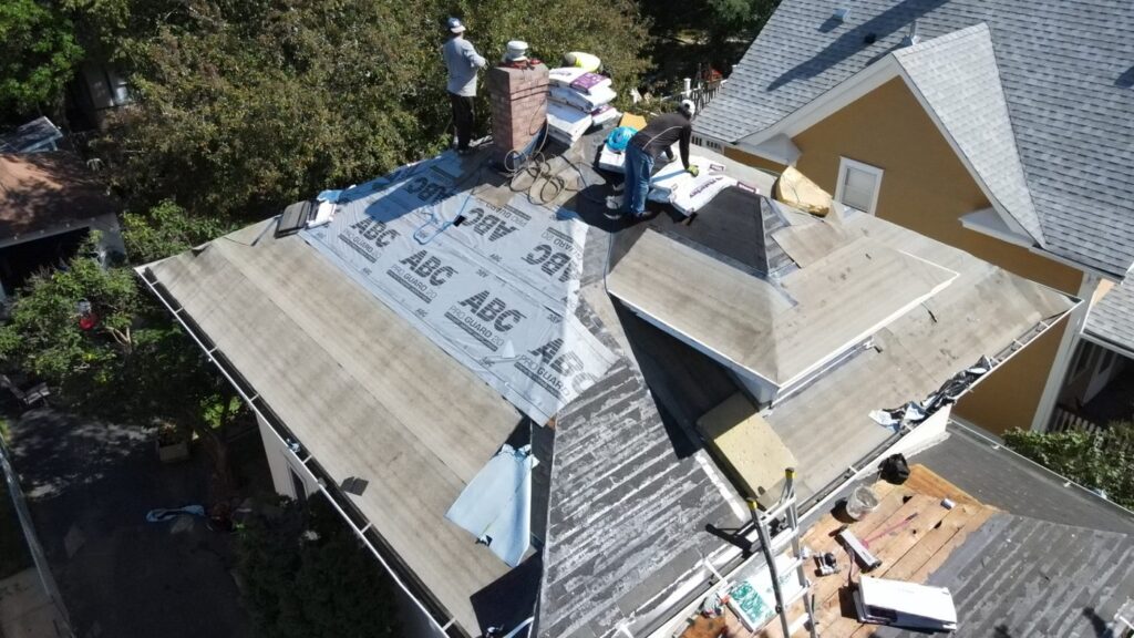 Roofing crew placing underlayment and preparing materials on a residential roof.