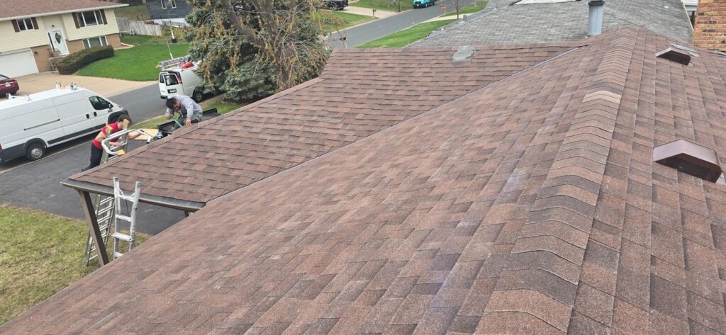 Roofing crew working along the edge of a brown shingle roof.